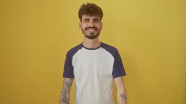Neşeli genç İspanyol adam, gülümsüyor ve altı parmağıyla güvenle işaret ediyor, izole edilmiş sarı arka planda duruyor, mutlu bir şekilde altı numarayı gösteriyor.