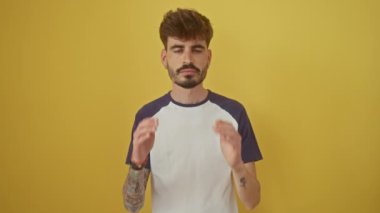 Migren ağrısı çeken genç İspanyol bir adam, sarı arka planda izole bir şekilde duruyor, acı ve başıyla strese giriyor.