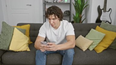 Kıvırcık saçlı İspanyol adam rahat oturma odasında akıllı telefondan selfie çekiyor..