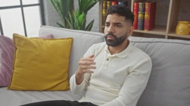 Genç İspanyol adam evde, elini uzatıp ağzını kapatıyor, uykusuzluk ve sıkıntı belirtileri gösteriyor, yorgun ve huzursuz.