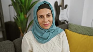 Başörtüsü takan neşeli, olgun bir kadın sıcak bir oturma odasında gözlüklerle poz verir, sıcaklığı ve kişiliği yayar..