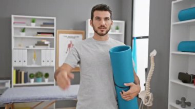 Stresli genç İspanyol bir adam, elinde yoga minderiyle rehabilitasyon kliniğinde, hayal kırıklığını yönlendiriyor ve öfkeyle şaşırtıyor.