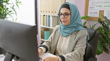 Başörtüsü takan profesyonel bir kadın ofis masasında bitkilerle çevrili meditasyon yapar..