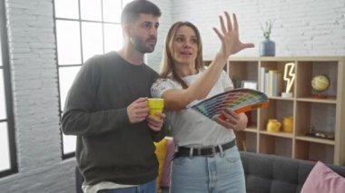 Bir erkek ve kadın, modern bir oturma odasında kumaş bir kitapla renk seçeneklerini tartışıyor ve ortak bir ev yenileme teması sunuyorlar..