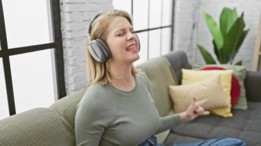Sarışın kadın, hoş bir oturma odasında kulaklıkla müzik dinlemekten hoşlanıyor..