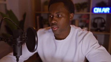 Odaklanmış Afro-Amerikan bir adam gece rahat bir stüdyodan podcast yapıyor..