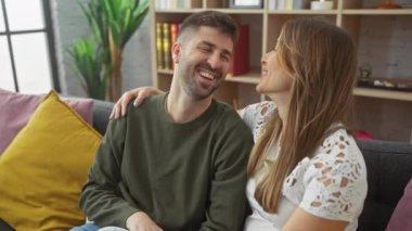 Neşeli bir adam ve kadın, iyi ışıklandırılmış bir oturma odasında, bir kanepede yan yana oturur, sevgi dolu bir anı paylaşırlar..