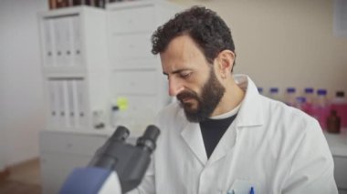 Olgun bir bilim adamı, laboratuvar ortamında güvenlik gözlüğü ve eldiven takmış bir numuneyi mikroskop altında inceliyor..