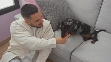 Genç bir İspanyol erkeği evdeki gri bir kanepede daksunduyla sevgiyle etkileşime geçer..
