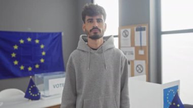 Sakallı genç bir adam, Avrupa seçim merkezinde arka planında Avrupa pankartı olan bir eu bayrağı taşıyor..