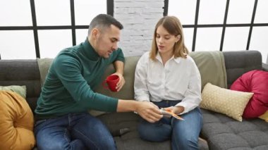 Bir erkek ve bir kadın, rahat bir oturma odasında, bir kumaş parçasının renklerini tartışarak, bir ev ortamında işbirliği ve seçim duygusunu aktararak, bir kanepeye yakın otururlar..