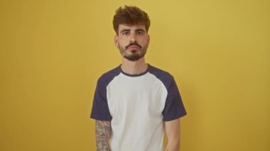 Neşeli, genç İspanyol bir adam seksi bir göz kırpma ile sarı izole bir arka planda mutluluğu ifade ediyor, kamerayla şakalaşıyor..