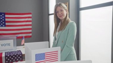 Genç yetişkin bir kadın, Amerikan bayraklarıyla dolu bir Amerikan üniversitesi seçim odasında başparmak kaldırırken gülümsüyor..