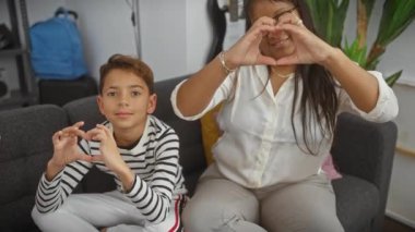 Bir kadın ve çocuk kalp şeklinde eller yapar, sıcak bir oturma odasında sevgi gösterirler.