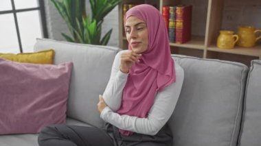 Düşünceli, tesettürlü genç İspanyol bir kadın, elleri çenesinde, koltukta oturuyor, kafa karıştırıcı bir soruyla boğuşuyor. Kafa karıştırıcı bir fikir göz önüne alındığında ciddi yüz derin düşünceleri yansıtır..