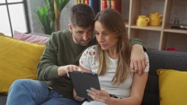 Sevgi dolu bir çift, kadın ve erkek, rahat bir oturma odasında tabletle birlikte uzanıyorlar..