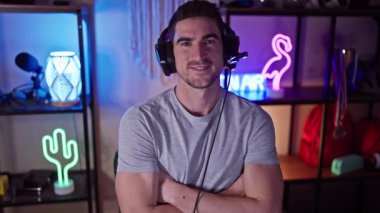 Kollarını çapraz bağlayan yakışıklı bir adam oyun odasında kulaklık takıyor ve geceleri neon ışıkları yanıyor..