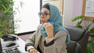Ofiste akıllı telefon kullanan tesettürlü profesyonel bir kadın..