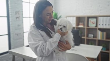 Gülümseyen genç bir kadın veteriner, veteriner kliniğinde sevimli bir bizon köpeğini kucaklıyor..