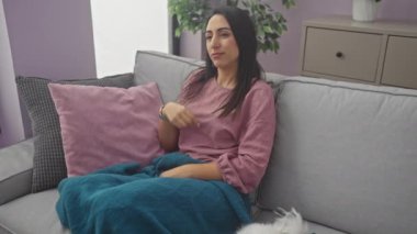 İspanyol kadın rahat oturma odasında beyaz köpeğiyle kanepede dinleniyor.