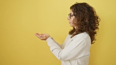 Gözlüklü neşeli, orta yaşlı İspanyol bir kadın, heyecanlı bir şekilde avuç içi açık bir şekilde ilan veriyor, fotokopi alanını gösteriyor, sarı arka planda tek başına duruyor, ürününüzü göstermekten mutlu.!