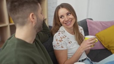 Bir erkek ve kadın sıcak bir şekilde yakınlaşır, rahat bir oturma odasında içkilerini paylaşır, rahat ve evcil bir atmosfer yayarlar..