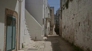 Güneşli bir günde yaşlanmış beyaz taş evlerle çevrili, Ostuni, Puglia, İtalya 'da dar, boş bir ara sokak. İtalyan mimari cazibesi ve dingin bir ortam yayıyor..
