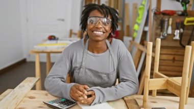 Saçları rastalı gülümseyen genç siyah kadın, parmak ile mükemmel bir sembol, güvenli gözlüklerle marangozlukta çalışıyor, neşe saçıyor ve başarıya ulaşıyor.