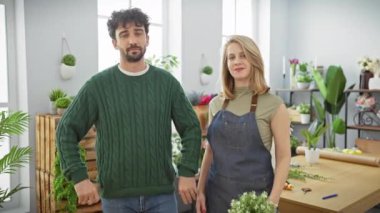 Kendine güvenen erkek ve kadın çiçekçiler. Parlak, bitkilerle dolu bir çiçekçide çapraz kolları olan.