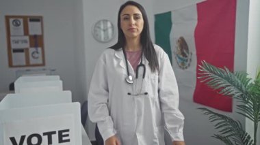 Beyaz laboratuvar önlüklü genç bir İspanyol kadın Meksika 'da bir seçim merkezinde arka planda bir bayrak ile kollarını kavuşturuyor..