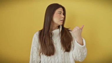 Süveter giyen, ağzı açık, tatlı bir şaşkınlık içinde, şaşırtıcı bir şekilde izole edilmiş sarı bir arkaplanı işaret eden göz kamaştırıcı genç İspanyol kadın..