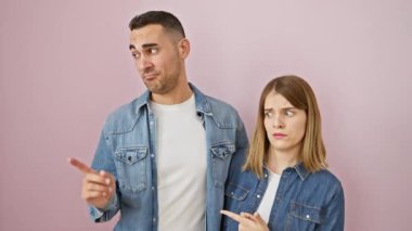 Şok olmuş kot gömlekli güzel çift endişeli bir şekilde pembe arka plan üzerinde kenara işaret, endişe ve şaşkınlık ifade, endişe kaynaşmış ayakta