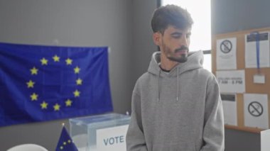 Yakışıklı bir İspanyol genç adam, arkasında bir eu bayrağıyla düşünceli bir şekilde bir Avrupa seçim merkezinde duruyor..