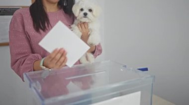 Küçük beyaz köpeğiyle kapalı bir seçim odasında oy kullanan genç bir İspanyol kadın..