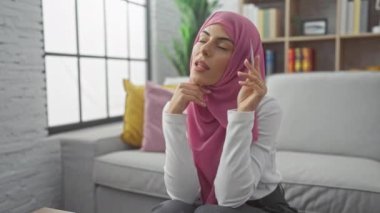 Başörtüsü takan düşünceli bir kadın evde oturur, elinde bir kredi kartı tutar, potansiyel olarak satın almayı düşünür..