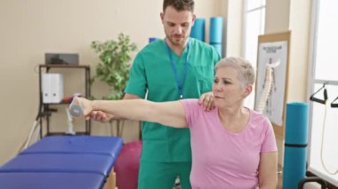 Bir kadın, erkek fizyoterapist gibi halterle egzersiz yapıyor rehabilitasyon kliniğinde ona yardım ediyor..