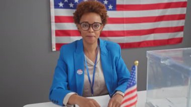 Neşeli Afro-Amerikan kadın hükümet adayı seçmen koleji afişini işaret ediyor, bulaşıcı neşeyle gülümsüyor.