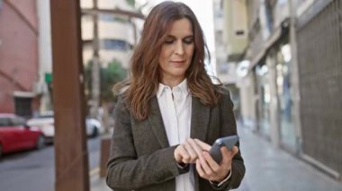 Şehir caddesinde akıllı telefon kullanan orta yaşlı bir kadın.