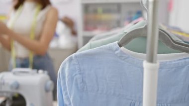 Çeşitli tekstil ürünleriyle dolu modern bir atölyede akıllı telefon kullanan odaklanmış bir kadın terzi..