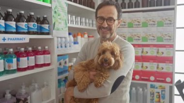 Sağlık ürünleri ve takviyelerle dolu bir eczanenin içinde kaniş köpeği tutan İspanyol bir adam..