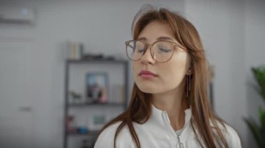 Evde, gözlüklü, sakin, nötr bir geçmişi olan genç bir kadının portresi..