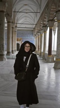 İstanbul 'da süslü bir caminin içinde gözlüklü ve tesettürlü bir kadın duruyor..