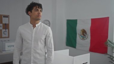 Yakışıklı, genç, İspanyol bir adam Meksika 'da arka planda Meksika bayrağı olan bir oy kabininde düşünceli bir şekilde duruyor..