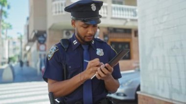 Odaklanmış Afro-Amerikan polisi şehir sokaklarında tablet kullanıyor.