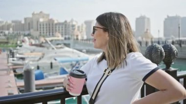 Bulanık bir marinayla kahve içen düşünceli bir kadının portresi ve Doha 'da mimari, Katar arka plan olarak..