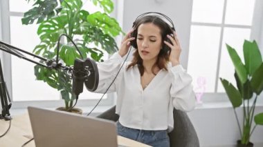 Modern bir stüdyoda dizüstü bilgisayarı ve mikrofonuyla podcast yapan İspanyol kadın..