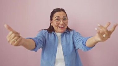 Neşeli orta yaşlı İspanyol kadın, kolları açık sevgi dolu bir kucaklaşma için, canlı pembe izole bir arka plan üzerinden kameraya ışıldıyor..