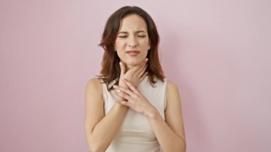 Genç, güzel İspanyol bir kadının yürek burkan portresi, soyutlanmış pembe bir duvarın önünde duruyor, eli boğazında ve boynunda, acı verici grip belirtileri, enfeksiyon, hastalık belirtileri..