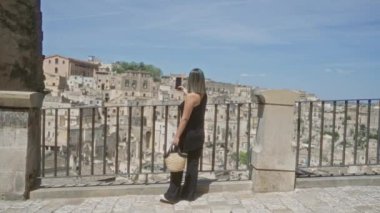 Siyah elbiseli genç İspanyol bir kadın elinde kamış torbayla, tarihi eski kasabanın panoramik manzarasının tadını çıkarıyor. Materyalist, basilicata, açık gökyüzü ile İtalya 'nın manzarası..