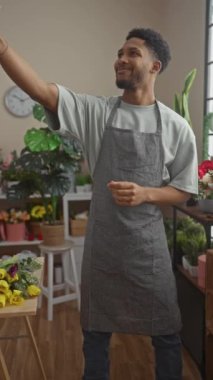 Önlüklü gülen adam çiçekçi dükkanında yemyeşil ve canlı bitkilerle selfie çekiyor..